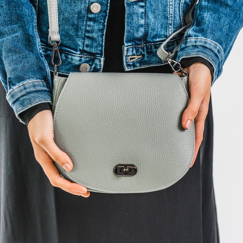 Dove grey soft pebbled leather ladies saddle handbag. Oxidised hardware, adjustable strap, use as a crossbody or shoulder bag, detachable straps, fully lined, can be personalised with an engraved disc.