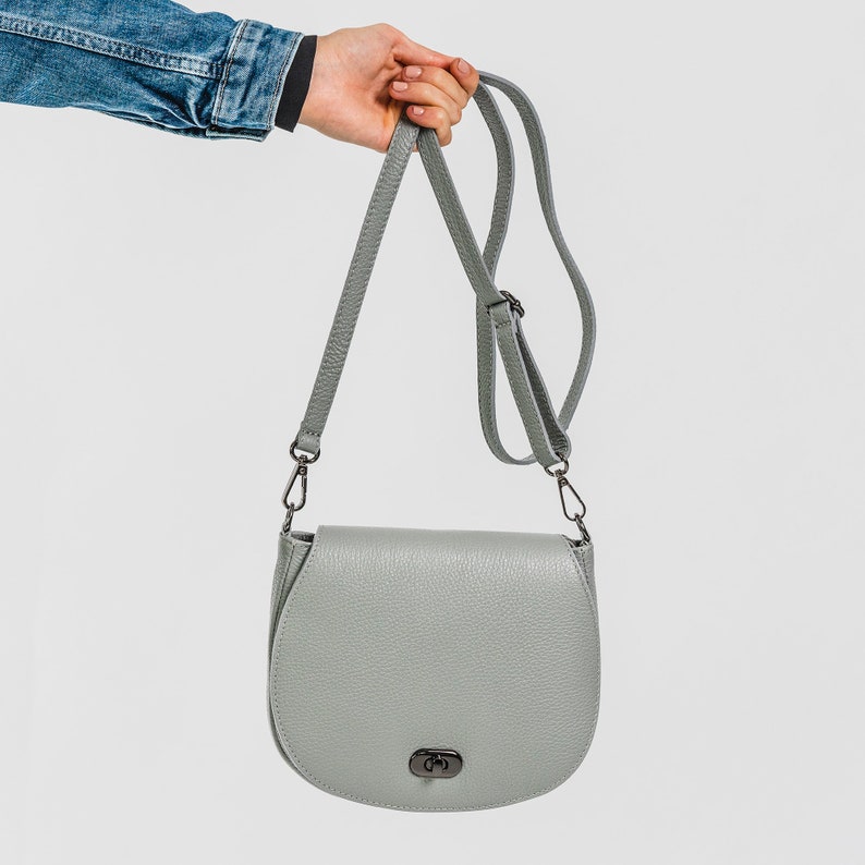 Dove grey soft pebbled leather ladies saddle handbag. Oxidised hardware, adjustable strap, use as a crossbody or shoulder bag, detachable straps, fully lined, can be personalised with an engraved disc.