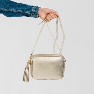 Metallic gold soft pebbled leather ladies box handbag. With gold hardware, tassel close, adjustable strap, use as a crossbody or shoulder bag, detachable straps, fully lined, can be personalised with an engraved disc.