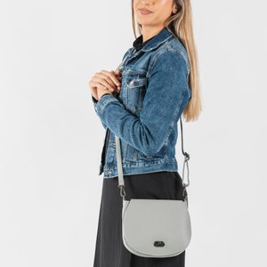 Dove grey soft pebbled leather ladies saddle handbag. Oxidised hardware, adjustable strap, use as a crossbody or shoulder bag, detachable straps, fully lined, can be personalised with an engraved disc.