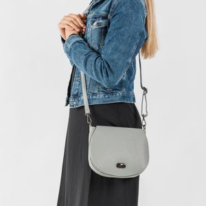 Dove grey soft pebbled leather ladies saddle handbag. Oxidised hardware, adjustable strap, use as a crossbody or shoulder bag, detachable straps, fully lined, can be personalised with an engraved disc.