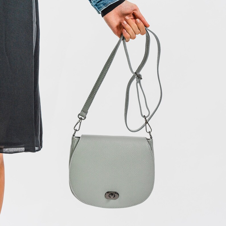 Dove grey soft pebbled leather ladies saddle handbag. Oxidised hardware, adjustable strap, use as a crossbody or shoulder bag, detachable straps, fully lined, can be personalised with an engraved disc.