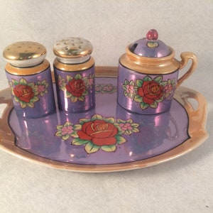 Lote de 4 piezas de porcelana con estampado floral de rosas en tonos morados y naranjas: salero y pimentero, bandeja y azucarero.