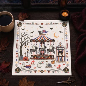 May include: A square cross-stitch pattern featuring a Halloween-themed carousel with ghosts riding skeleton horses, a ticket booth, a black cat, pumpkins, bats, and a crescent moon, all framed by a decorative border with small skulls and moons.