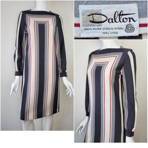 May include: A gray and white striped dress with a red stripe detail. The dress has a square neckline and long sleeves. The dress is made of 100% pure virgin wool and has a Dalton label with the text "WPL 11765".