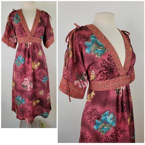 May include: A vintage floral print dress with a V-neckline and short sleeves. The dress has a burgundy background with a floral pattern in shades of pink, blue, and yellow. The dress has a tie detail at the shoulders and a fitted waist.