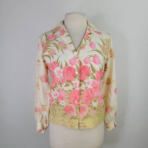 May include: A vintage button-up blouse with a floral print in shades of pink and green on a cream background. The blouse has long sleeves and a collared neckline.