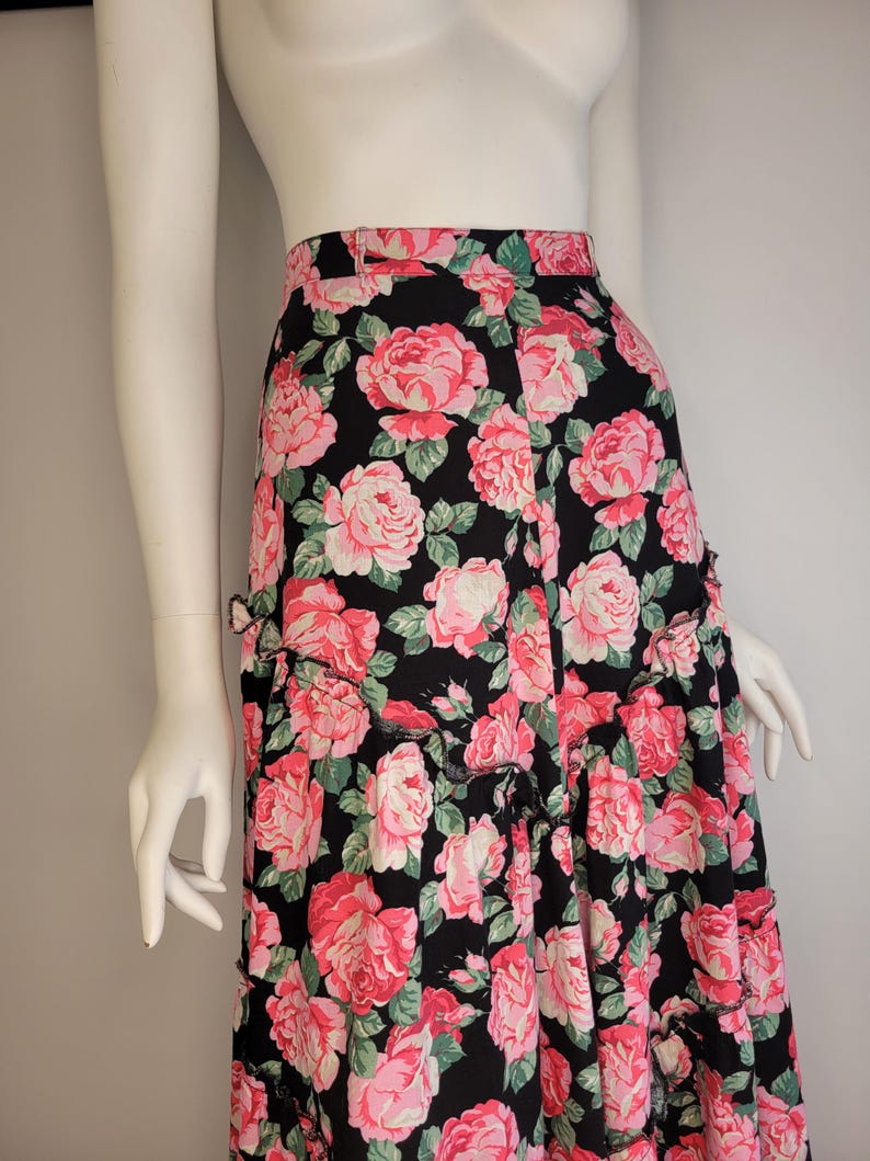 May include: A black maxi skirt with a pink and green floral print. The skirt has a ruffled hem and a fitted waist.