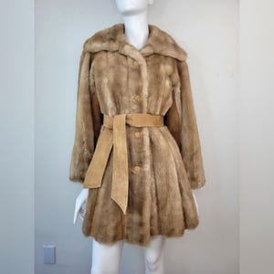 Peut inclure: Manteau vintage en fausse fourrure marron, présenté sur un mannequin. Le manteau a un large col, des boutons et une ceinture en daim assortie. La longueur du manteau s'étend jusqu'à mi-cuisse.