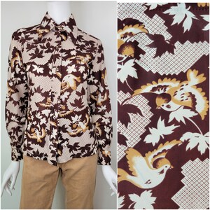 May include: A long-sleeved button-up shirt with a brown and white pattern of leaves and birds. The shirt has a large collar and a button-up front.