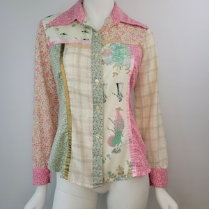 Puede incluir: Una camisa de manga larga con botones que presenta un diseño de patchwork con varios tejidos. La camisa incluye paneles con estampado floral rosa, tela color crema con cuadros verdes y tela color crema con figuras históricas.