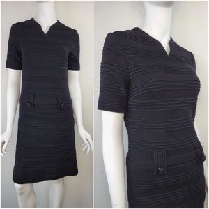 May include: A black ribbed knit dress with a v-neckline and short sleeves. The dress has a fitted silhouette and a straight hemline. It features two buttons on the front and two pockets on the sides.