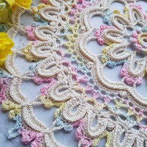May include: A delicate crocheted doily with a circular design in shades of pink, yellow, and blue.