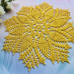 May include: A yellow crocheted doily with a delicate floral pattern. The doily is circular and has a lacy edge.