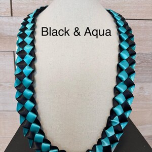 May include: A woven ribbon necklace in black and aqua blue, displayed on a mannequin. The text "Black & Aqua" is visible on the image. The necklace is made of satin ribbon and is designed in a braided pattern.