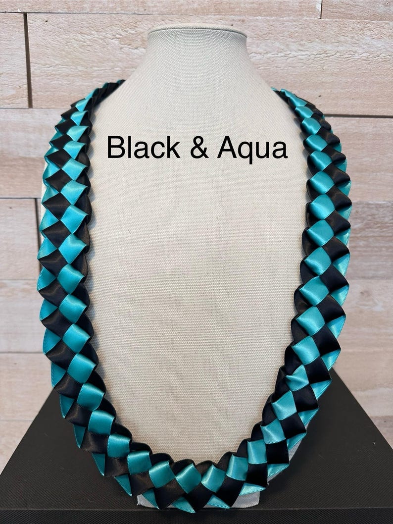 May include: A woven ribbon necklace in black and aqua blue, displayed on a mannequin. The text "Black & Aqua" is visible on the image. The necklace is made of satin ribbon and is designed in a braided pattern.