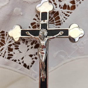 May include: A silver and black crucifix with a detailed depiction of Jesus Christ. The cross has a decorative, four-leaf clover design on the ends. The figure of Christ is in a silver tone, with intricate details.
