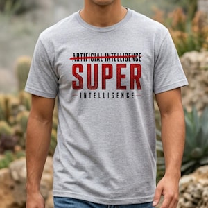 May include: A heather gray short-sleeve t-shirt featuring the text ARTIFICIAL INTELLIGENCE with a red line through it, the word SUPER in large red letters, and the word INTELLIGENCE below it, all centered on the chest of the garment.