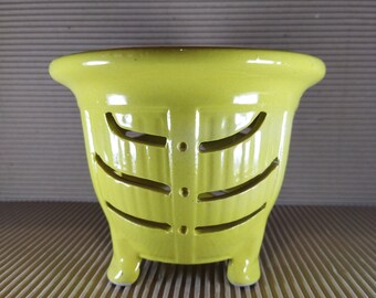 May include: A yellow ceramic planter with a decorative cut-out design and three legs.