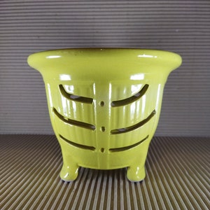 May include: A yellow ceramic planter with a decorative cut-out design and three legs.