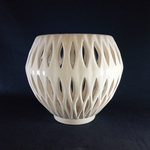 Peut inclure: Vase en céramique blanche avec un motif découpé décoratif. Le vase a une forme ronde et une large ouverture.