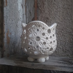 May include: White ceramic planter with a delicate, lacy design and four small feet. The planter has a circular opening at the top and is perfect for displaying small plants or flowers.