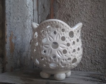 May include: White ceramic planter with a delicate, lacy design and four small feet. The planter has a circular opening at the top and is perfect for displaying small plants or flowers.