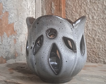 May include: A black and silver ceramic candle holder with a decorative cut-out design. The holder has a rounded shape and a textured surface.
