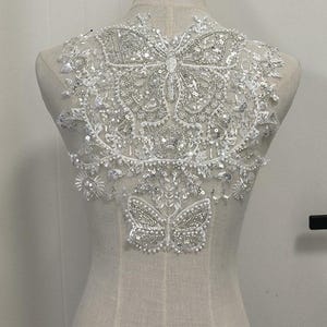 May include: A white lace applique with two large silver butterfly embellishments and a smaller silver butterfly embellishment at the bottom.