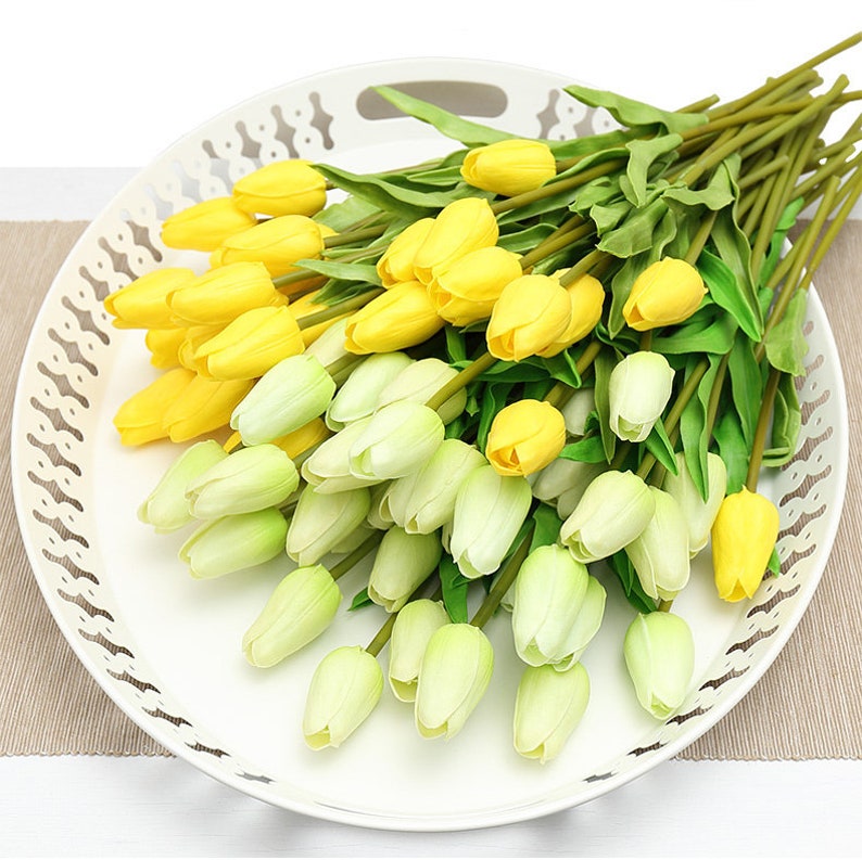 Op de afbeelding: Een boeket kunstmatige tulpen in een witte schaal. De tulpen zijn een mix van geel en lichtgroen.