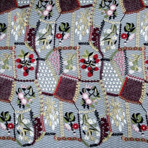 Puede incluir: Primer plano de una tela gris con un patr&oacute;n repetido de flores, hojas y espigas de trigo bordadas. El bordado est&aacute; en tonos de rojo, blanco, verde y marr&oacute;n.