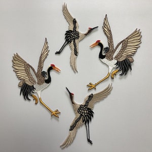 May include: Four embroidered iron-on patches of cranes in flight. The cranes are beige, white, and black with red accents.