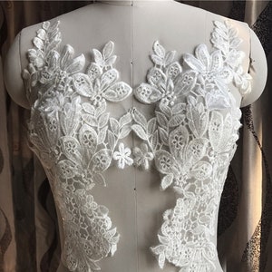 May include: White lace applique with floral designs. The lace is delicate and intricate, with a variety of flower shapes and sizes. This lace applique would be perfect for adding a touch of elegance to any project.