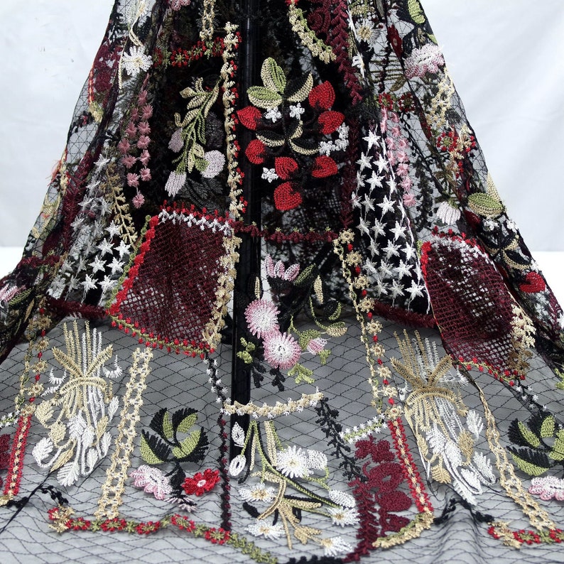 Puede incluir: Tela negra transparente con patrones florales y estrellas bordadas en rojo, blanco, verde y dorado.