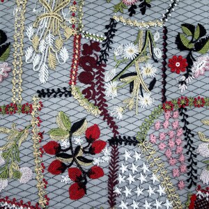 Puede incluir: Primer plano de un tejido bordado con un patr&oacute;n floral. El tejido es de color gris claro con una textura de malla fina. El bordado est&aacute; en tonos de rojo, verde, rosa y blanco.