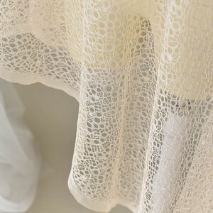 May include: Close-up of a white lace fabric with a circular pattern. The fabric is soft and delicate, with a subtle sheen.