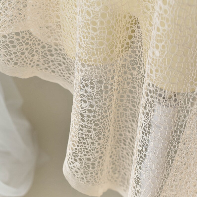 May include: Close-up of a white lace fabric with a circular pattern. The fabric is soft and delicate, with a subtle sheen.