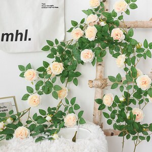 May include: Artificial rose vine with light pink flowers and green leaves. The vine is hanging on a wooden ladder. The text "Where there is life there is hope" and "Thank the sun rises again, continue to fight my dream" is visible on a white tote bag.