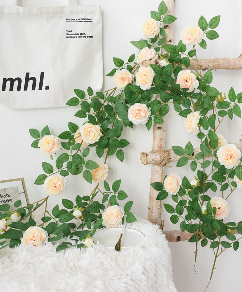 May include: Artificial rose vine with light pink flowers and green leaves. The vine is hanging on a wooden ladder. The text "Where there is life there is hope" and "Thank the sun rises again, continue to fight my dream" is visible on a white tote bag.