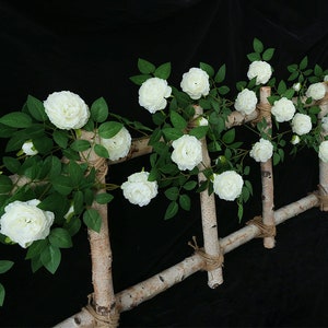 May include: White artificial rose vine with green leaves wrapped around a birch wood trellis. The vine is made of plastic and has a realistic look.