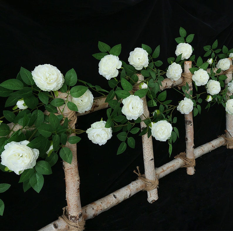 May include: White artificial rose vine with green leaves wrapped around a birch wood trellis. The vine is made of plastic and has a realistic look.
