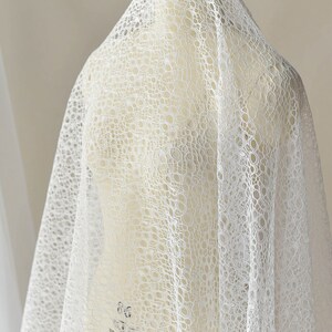 May include: White lace fabric with a circular pattern. The fabric is draped over a white dress form.