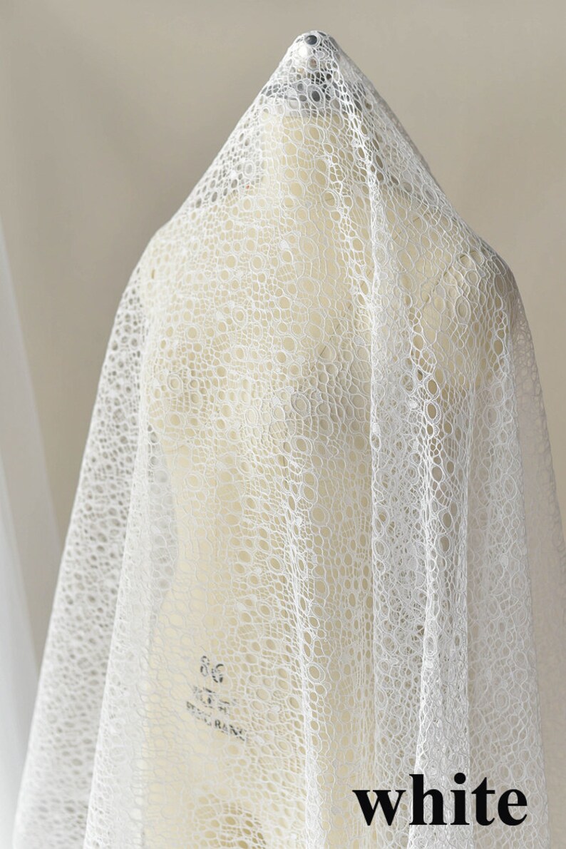 May include: White lace fabric with a circular pattern. The fabric is draped over a white dress form.