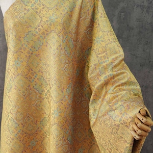 May include: A length of fabric featuring a repeating intricate pattern in shades of golden yellow, soft teal, and muted orange. The textile displays a dense, symmetrical design with ornate motifs that create a textured appearance across the surface.