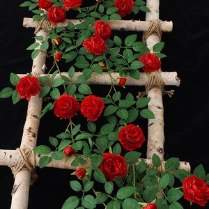 May include: Artificial red rose vine with green leaves wrapped around a birch wood ladder with twine.