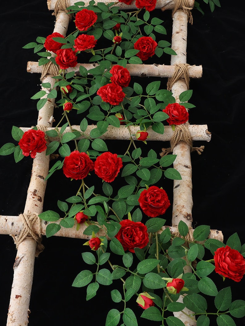 May include: Artificial red rose vine with green leaves wrapped around a birch wood ladder with twine.