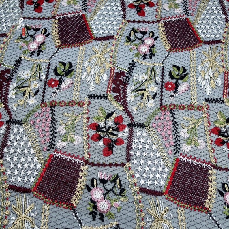 Puede incluir: Primer plano de una tela con un dise&ntilde;o de patchwork que presenta flores, hojas y bayas bordadas en tonos rojos, verdes, blancos y dorados. La tela tiene una textura delicada y de malla.