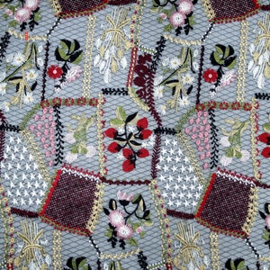 Puede incluir: Primer plano de una tela delicada bordada con un dise&ntilde;o de patchwork. La tela presenta una variedad de motivos florales en tonos rojos, rosas, verdes y blancos, sobre un fondo gris.