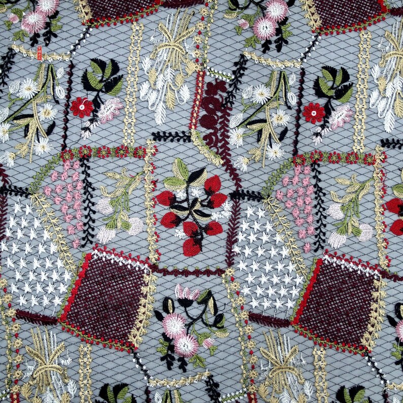 Puede incluir: Primer plano de una tela delicada bordada con un dise&ntilde;o de patchwork. La tela presenta una variedad de motivos florales en tonos rojos, rosas, verdes y blancos, sobre un fondo gris.