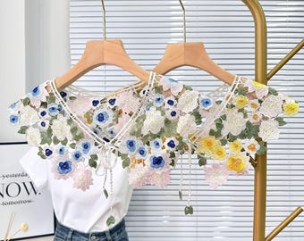 May include: Two white lace collars with floral embroidery. One collar features pink, blue, and green flowers, while the other features yellow, white, and green flowers.
